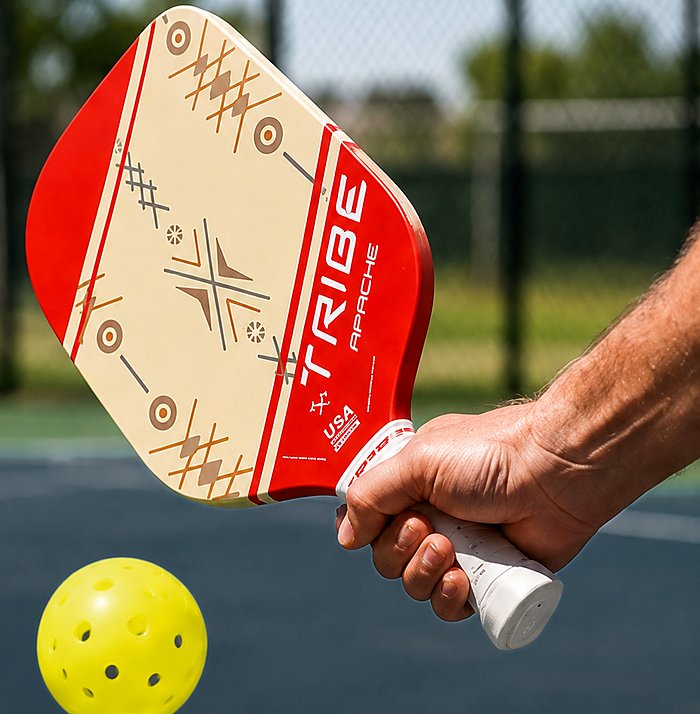 A player striking a pickleball with the TRIBE Apache on an outdoor court